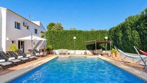 A swimming pool with lounge chairs and a pergola, surrounded by a white building and greenery. - Large and comfortable villa in Moraira, Costa Blanca, Spain  with heated pool for 12 persons (Moraira)