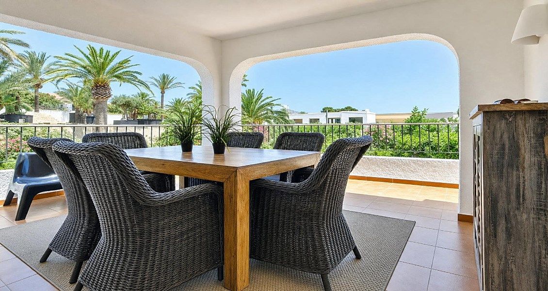 A dining area with a table and chairs, a view of palm trees, and a balcony railing.