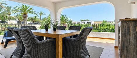A dining area with a table and chairs, a view of palm trees, and a balcony railing.