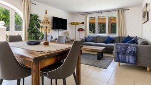 A living room with a sofa, a coffee table, a TV, and a dining area with chairs and a table. - Large and comfortable villa in Moraira, Costa Blanca, Spain  with heated pool for 12 persons (Moraira)