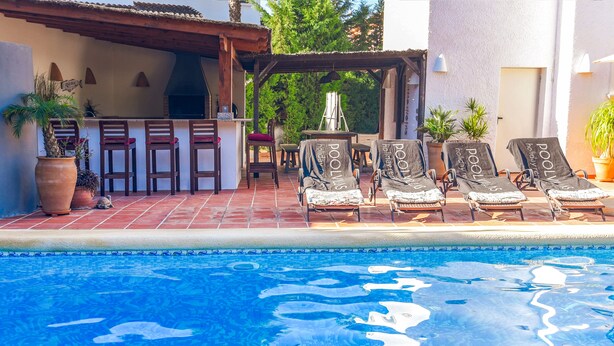 A pool area with lounge chairs, a bar, and potted plants.