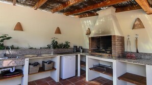 An outdoor kitchen with a brick oven, granite countertops, and a small refrigerator.