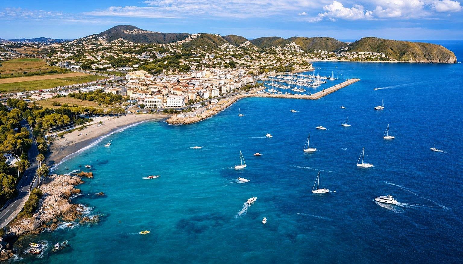 An aerial view of a coastal town with a marina, boats, and a mix of residential and commercial buildings.