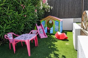 Un espace de jeux pour enfants avec un toboggan, deux chaises roses et une petite maison de jeu.