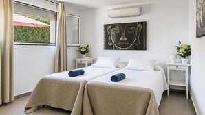 A hotel room with two beds, a window with curtains, a wall-mounted air conditioner, and a painting. - Large and comfortable villa in Moraira, Costa Blanca, Spain  with heated pool for 12 persons (Moraira)