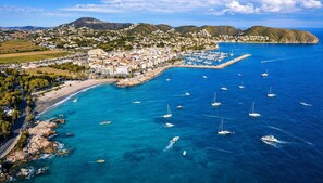 Vue aérienne d’une ville côtière avec un port de plaisance, des bateaux et un mélange de bâtiments résidentiels et commerciaux.