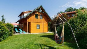A wooden house with a sloped roof, a swing chair, and a lawn with two lounge chairs. - Lovely apartment in villa for 4 guests with pool, WIFI, TV, terrace and pets allowed (Schlierbach)