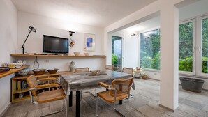 Un espace de repas moderne, doté d’une grande table, de chaises, d’un téléviseur et offrant une vue sur la verdure gr âce à de grandes fenêtres.