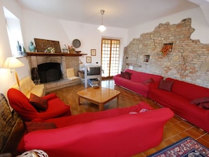 Un salón con chimenea, sofás rojos, un televisor y una pared de piedra.