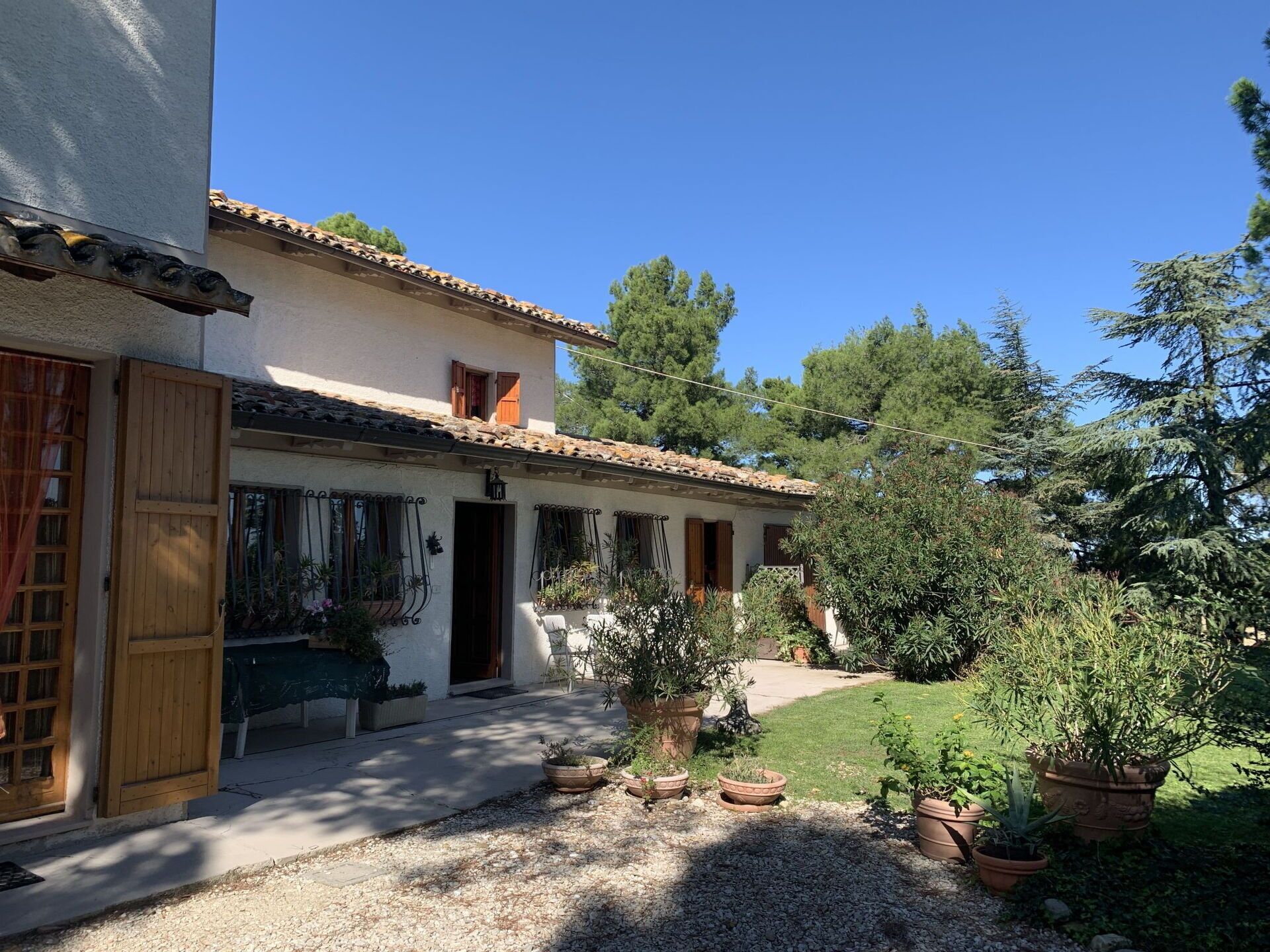 A two-story building with a tiled roof, a gravel driveway, and potted plants.