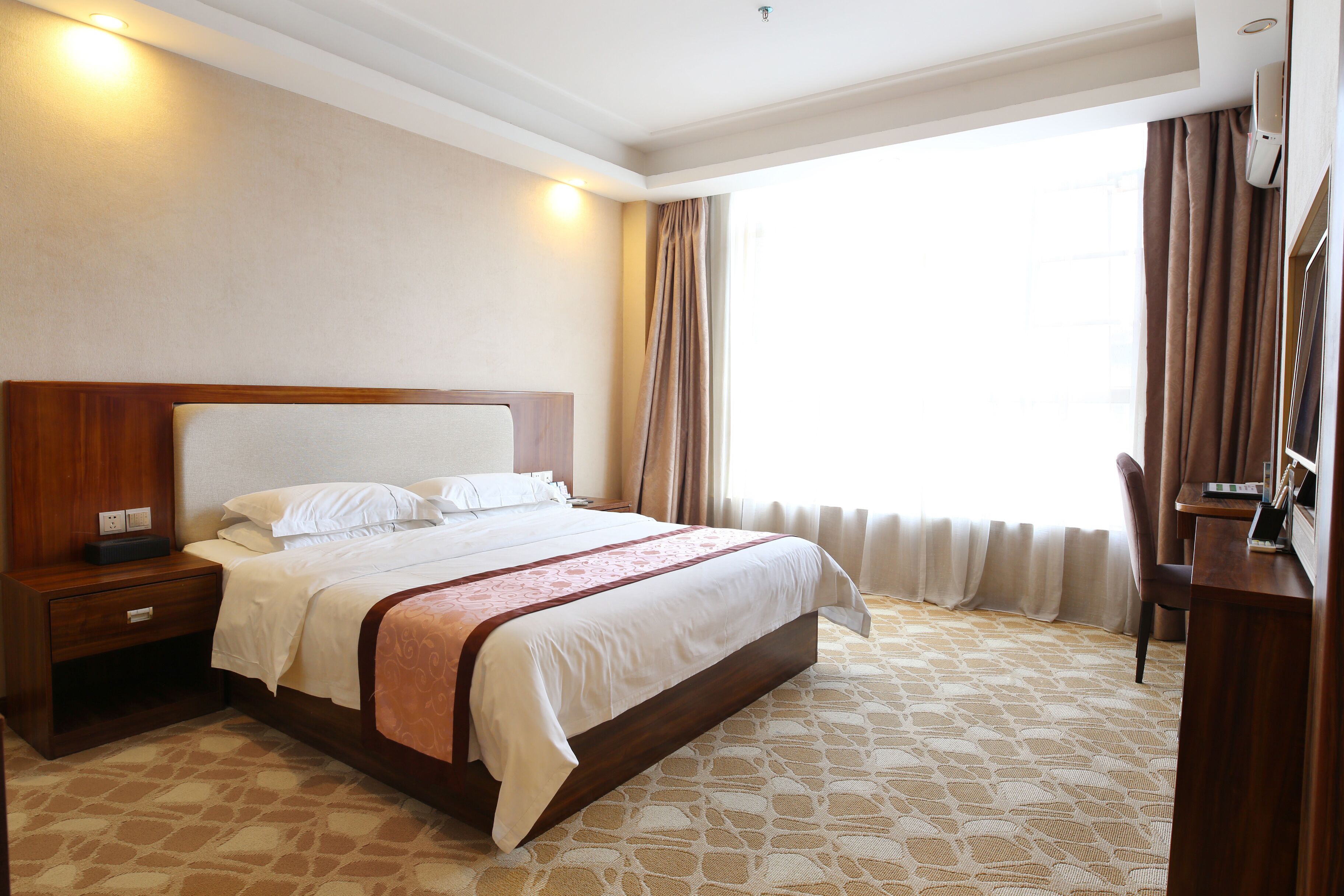 Una habitación de hotel con una cama grande, una mesita de noche de madera, un escritorio y una silla.