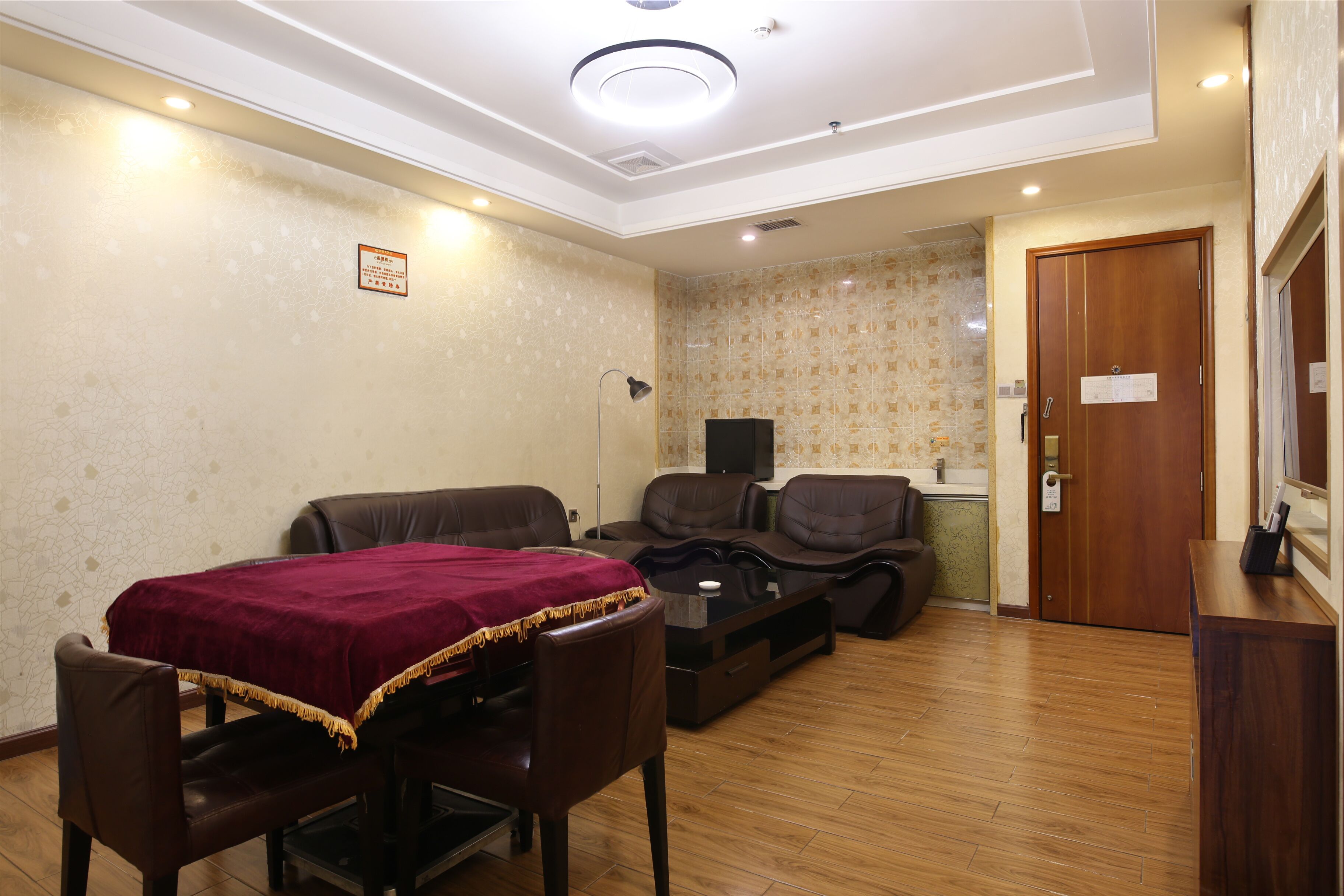 A room with a dining table, chairs, a sofa, and a massage chair. There is a wooden door and a small cabinet.