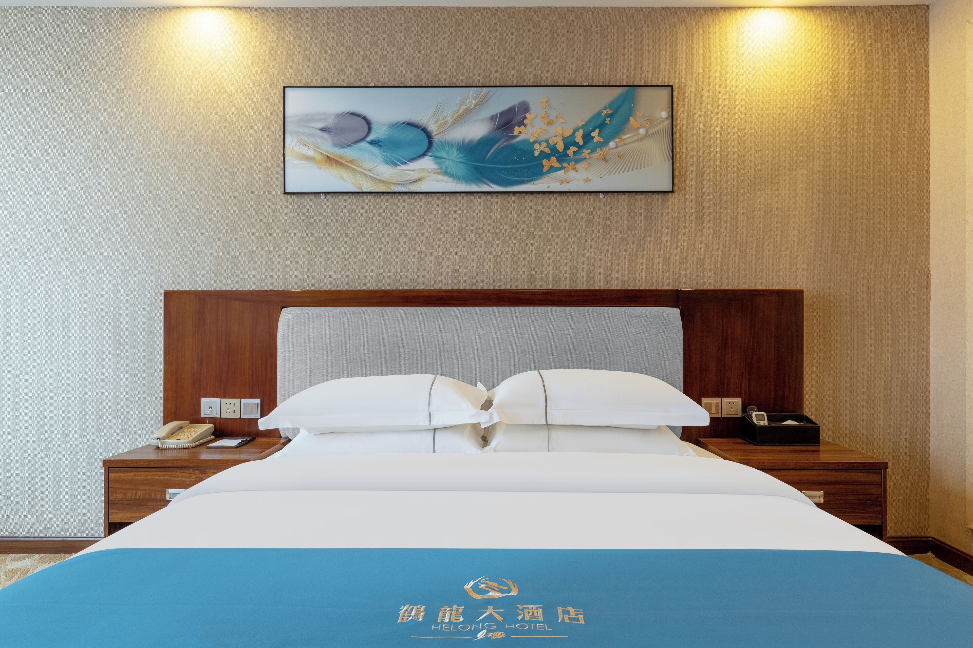 A hotel room with a neatly made bed, a bedside table with a phone and a lamp, and a wall-mounted artwork.