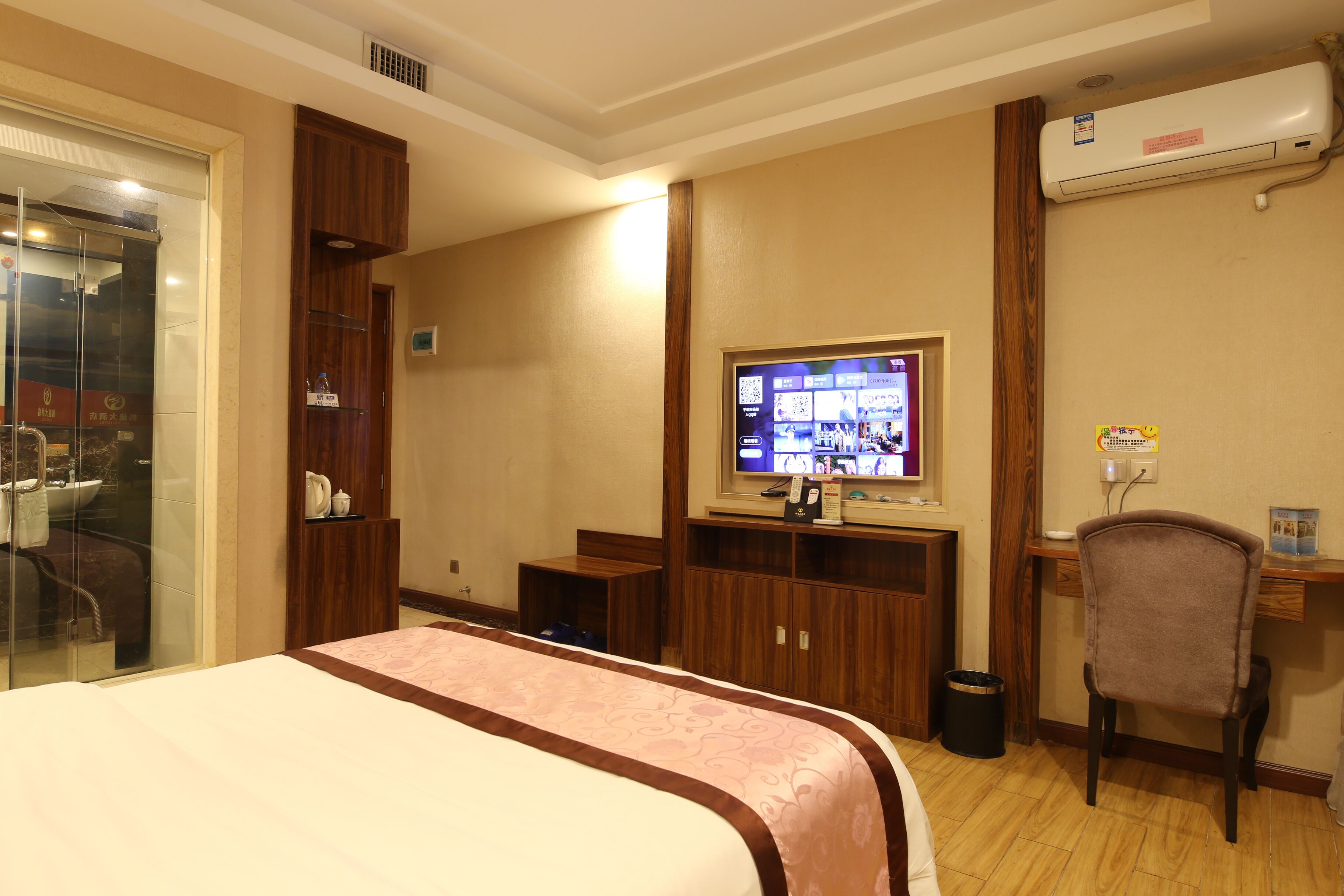 A hotel room with a bed, a desk, a chair, a television, and a bathroom with a glass shower enclosure.