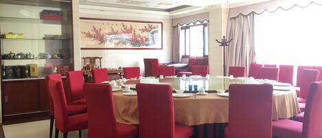 A dining area with round tables, red chairs, and a chandelier.