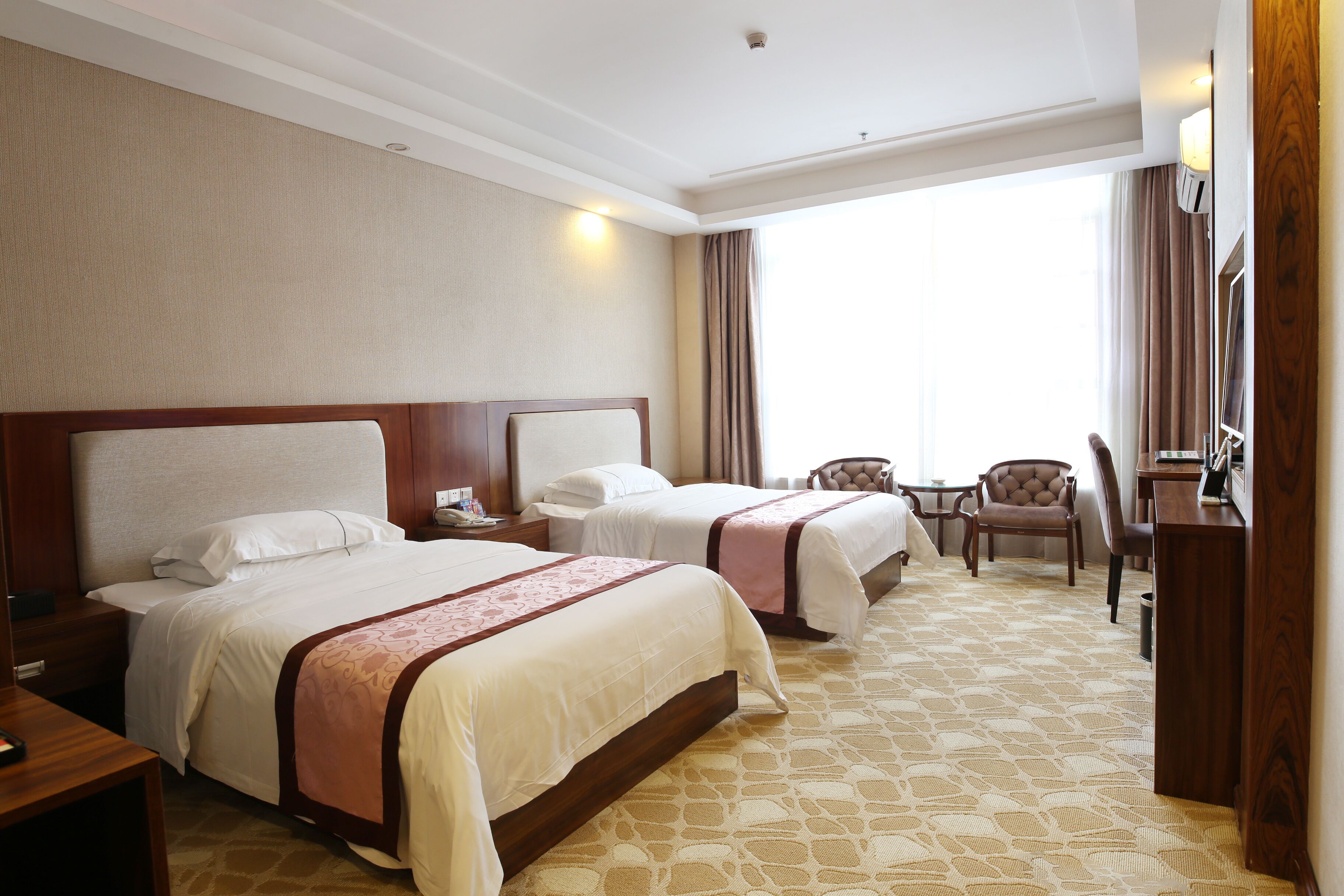 Une chambre d’hôtel avec deux lits, un bureau, une chaise et une grande fenêtre avec des rideaux.