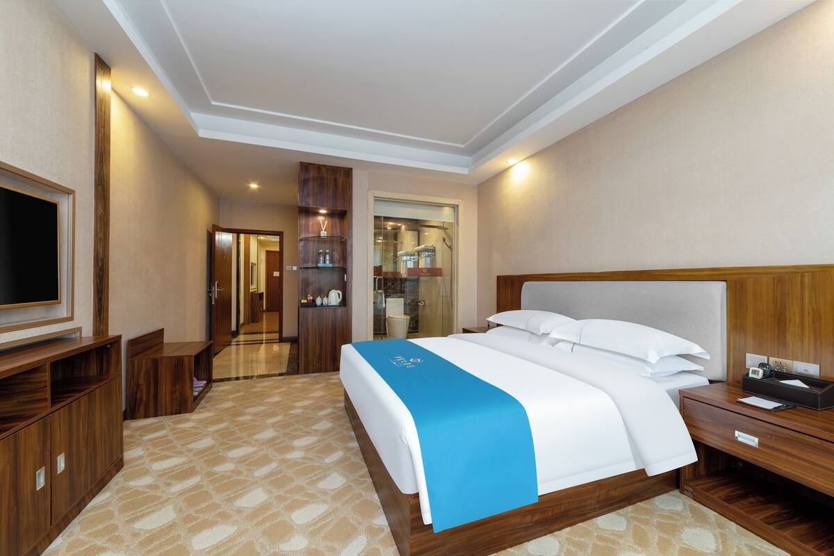 Hotelkamer met een groot bed, houten meubels, een televisie en een badkamer die door een open deur zichtbaar is.