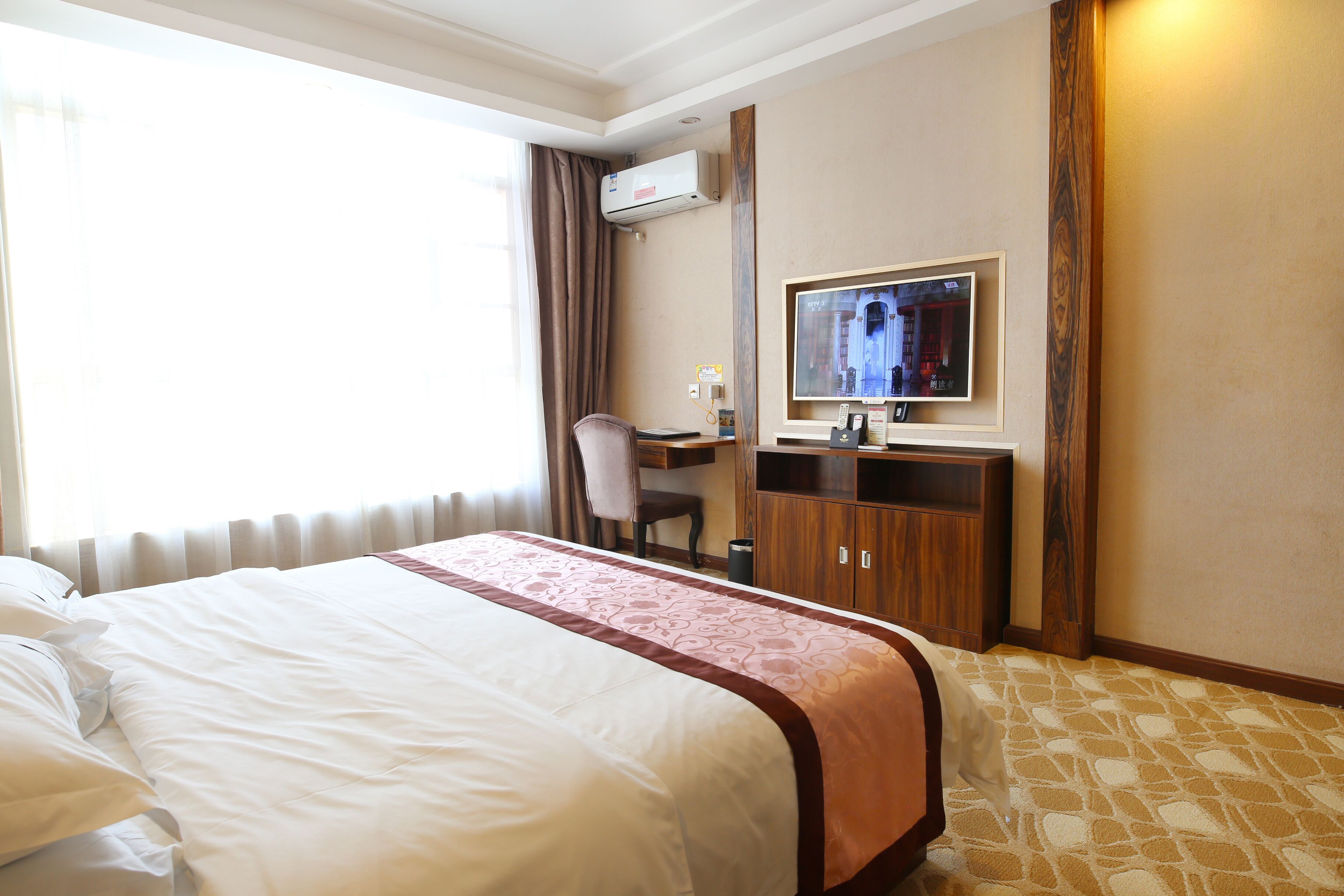 Een hotelkamer met een groot bed, een bureau met stoel, een televisie en een airconditioning.