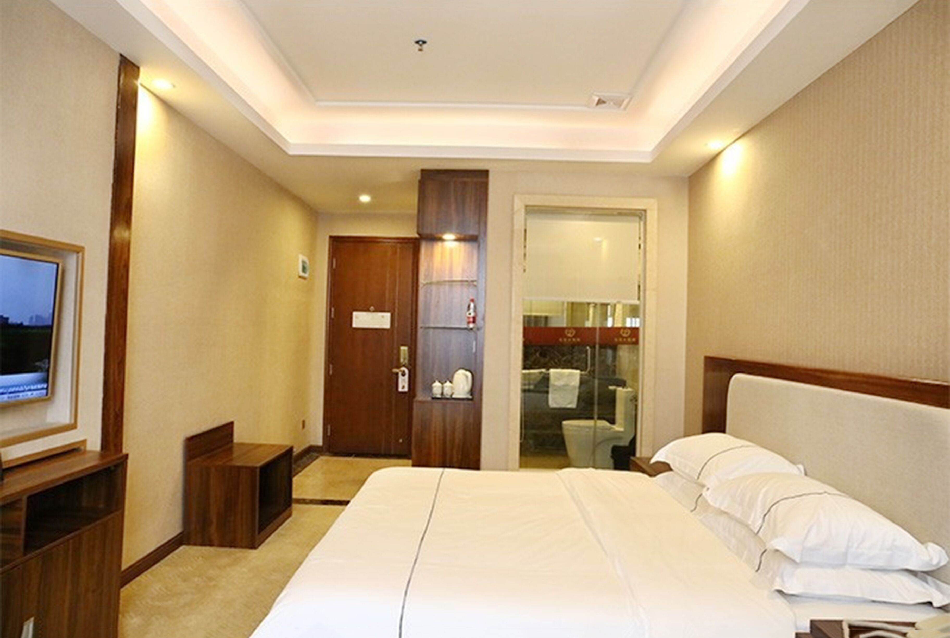 A hotel room with a large bed, a television on a wooden stand, a door leading to a bathroom, and a small seating area.