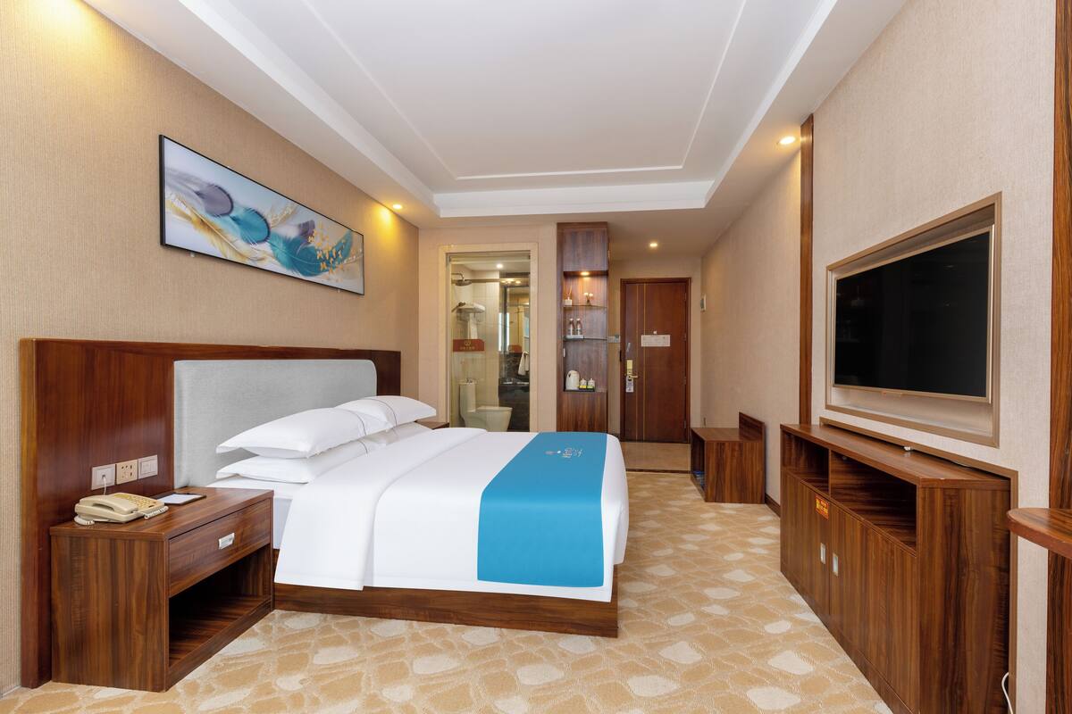 Een hotelkamer met een groot bed, een bureau met telefoon, een televisie en een badkamer die door een geopende deur zichtbaar is.