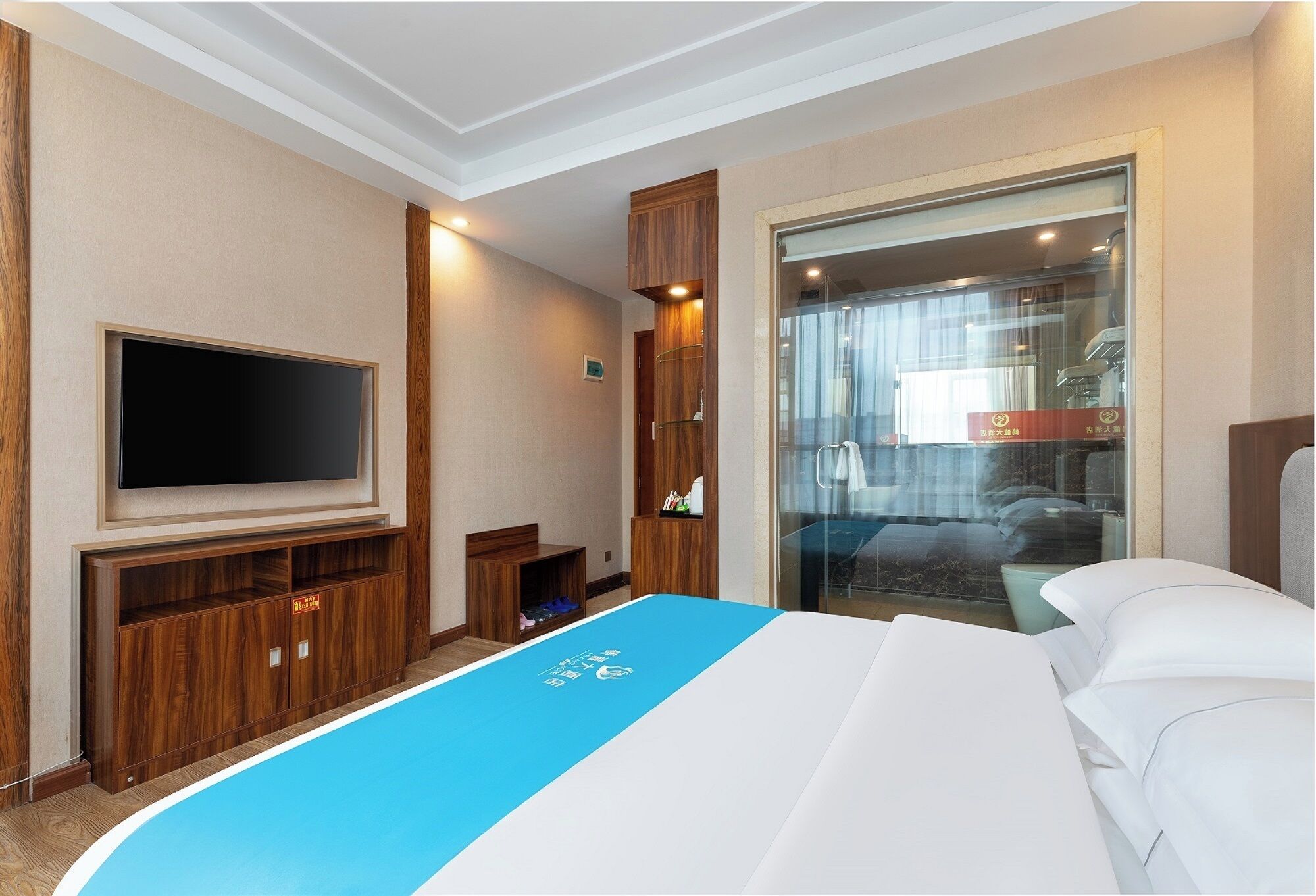 A hotel room with a large bed, a flat-screen TV, wooden furniture, and a glass door leading to a balcony.