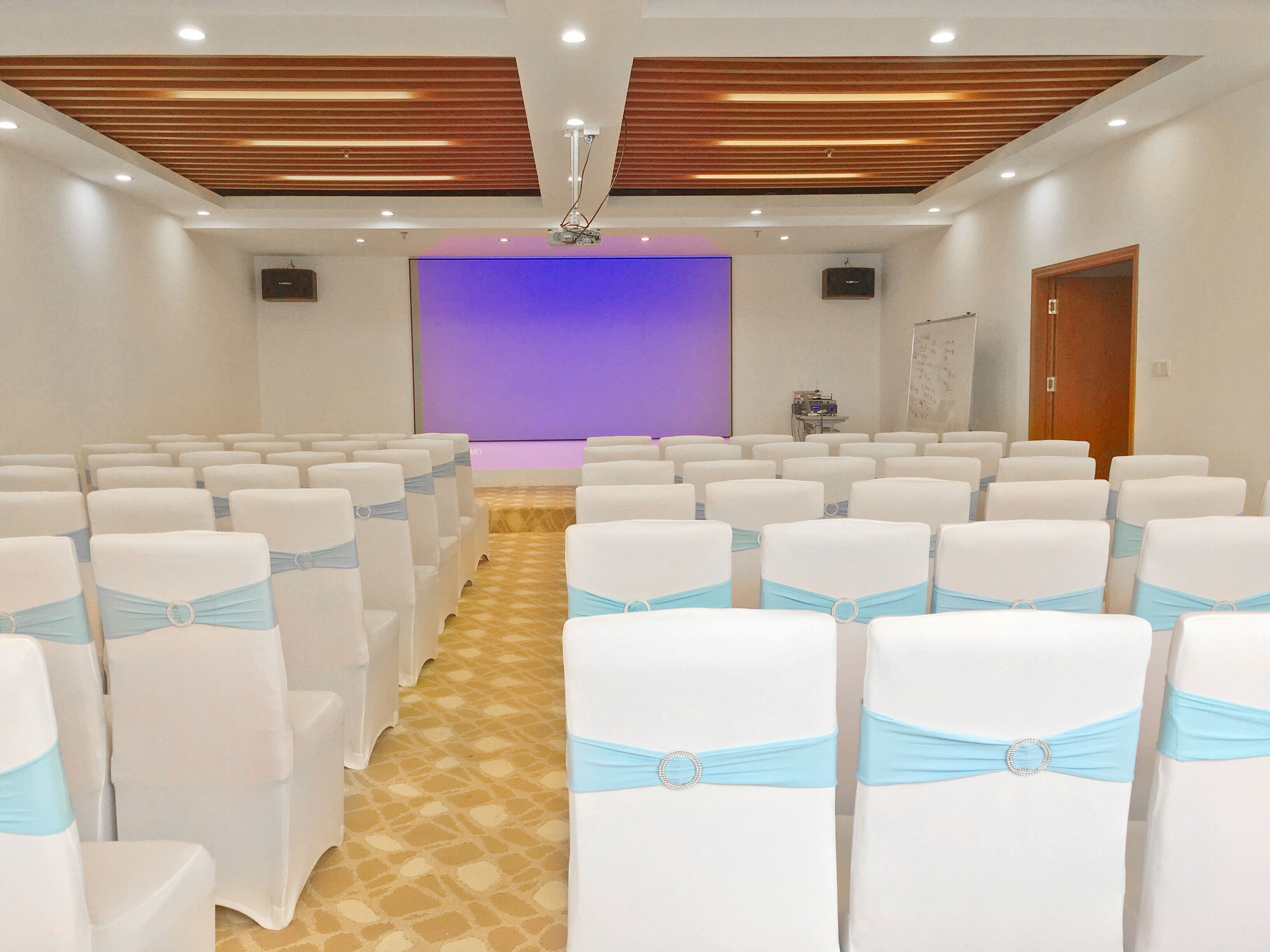 A conference room with rows of white chairs, each with a light blue sash, and a stage with a purple backdrop.