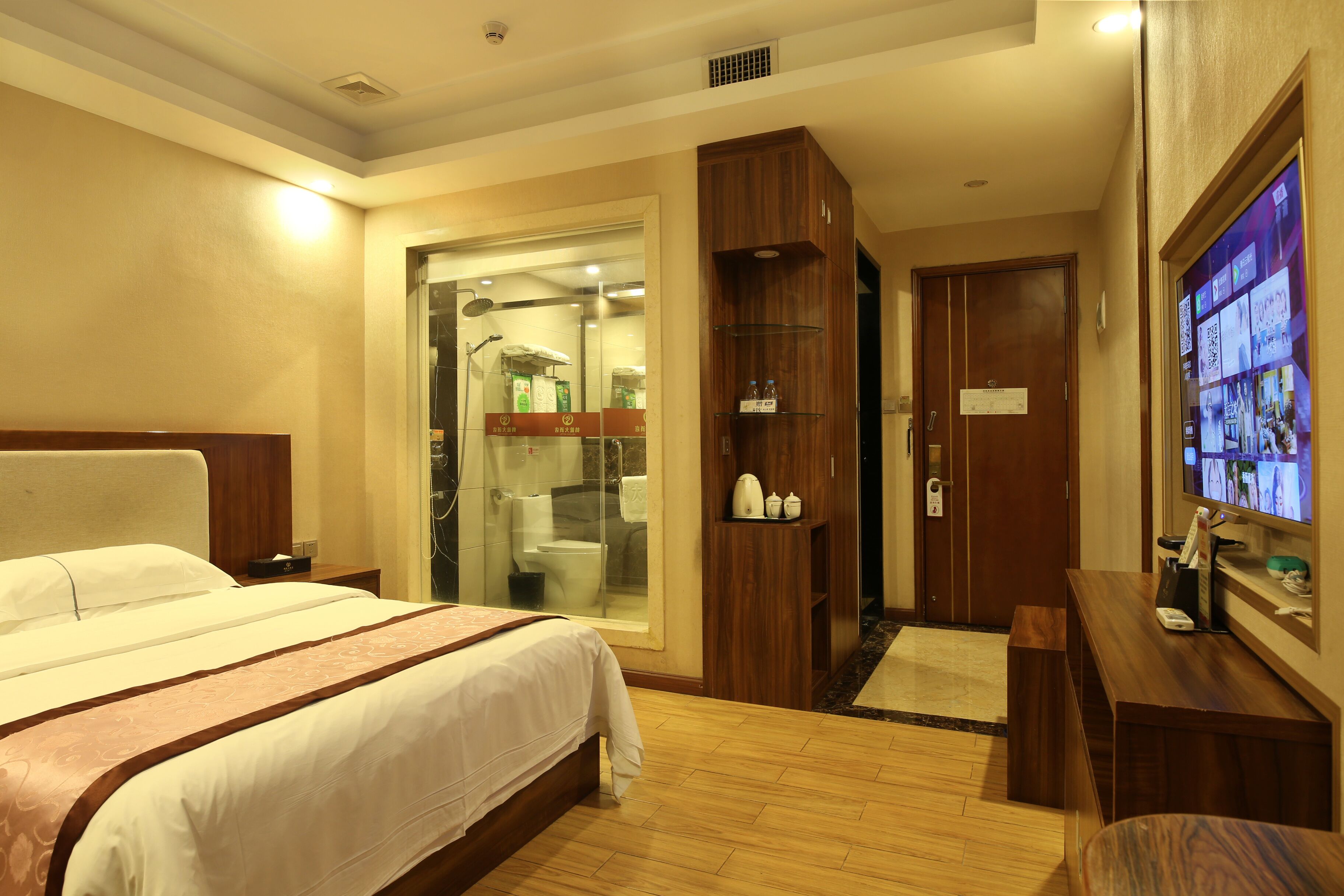 Habitación de hotel con cama, armario de madera, televisión y baño visible a través de una puerta de cristal.