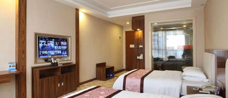 Habitación de hotel con dos camas, televisión, escritorio y baño visible a través de una puerta de vidrio.