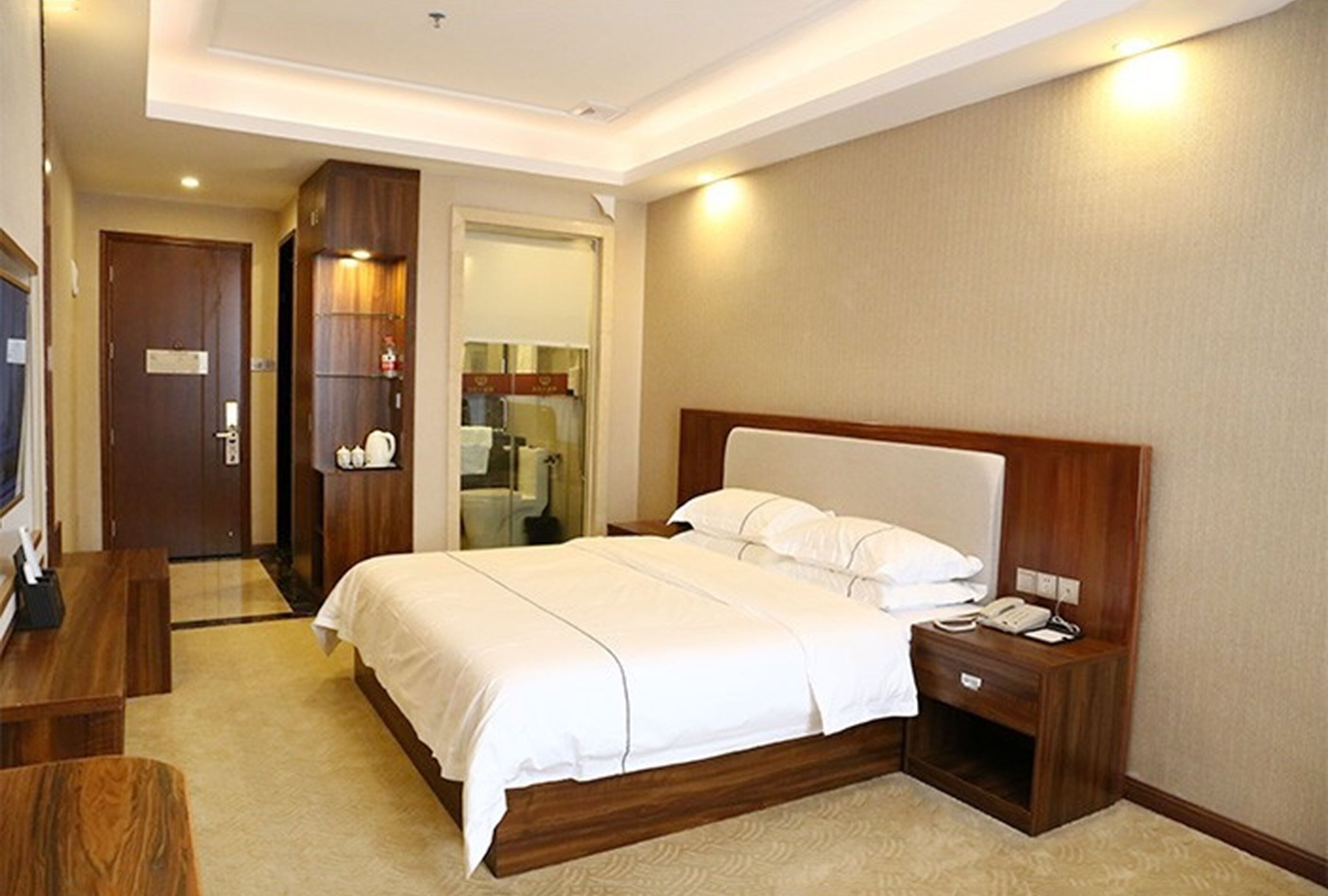 A hotel room with a large bed, bedside tables, a desk, and a wardrobe.