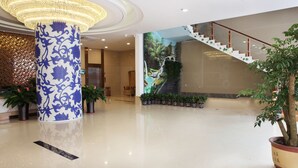 Un vestíbulo amplio con una gran columna decorativa, una escalera y plantas en macetas.