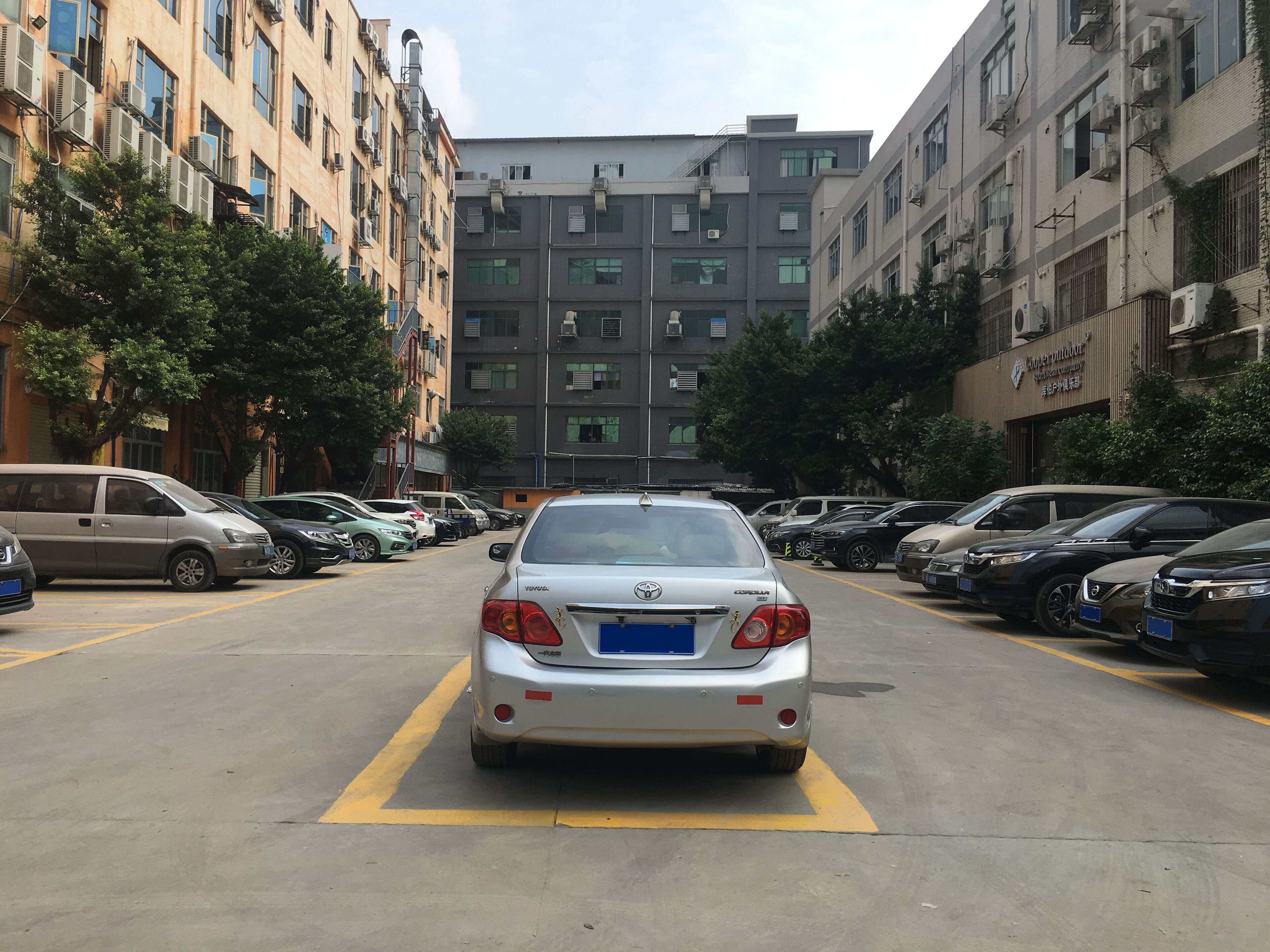 Een parkeerplaats met meerdere auto's in rijen, omringd door meer verdiepingen tellende gebouwen met balkons en airconditioners.