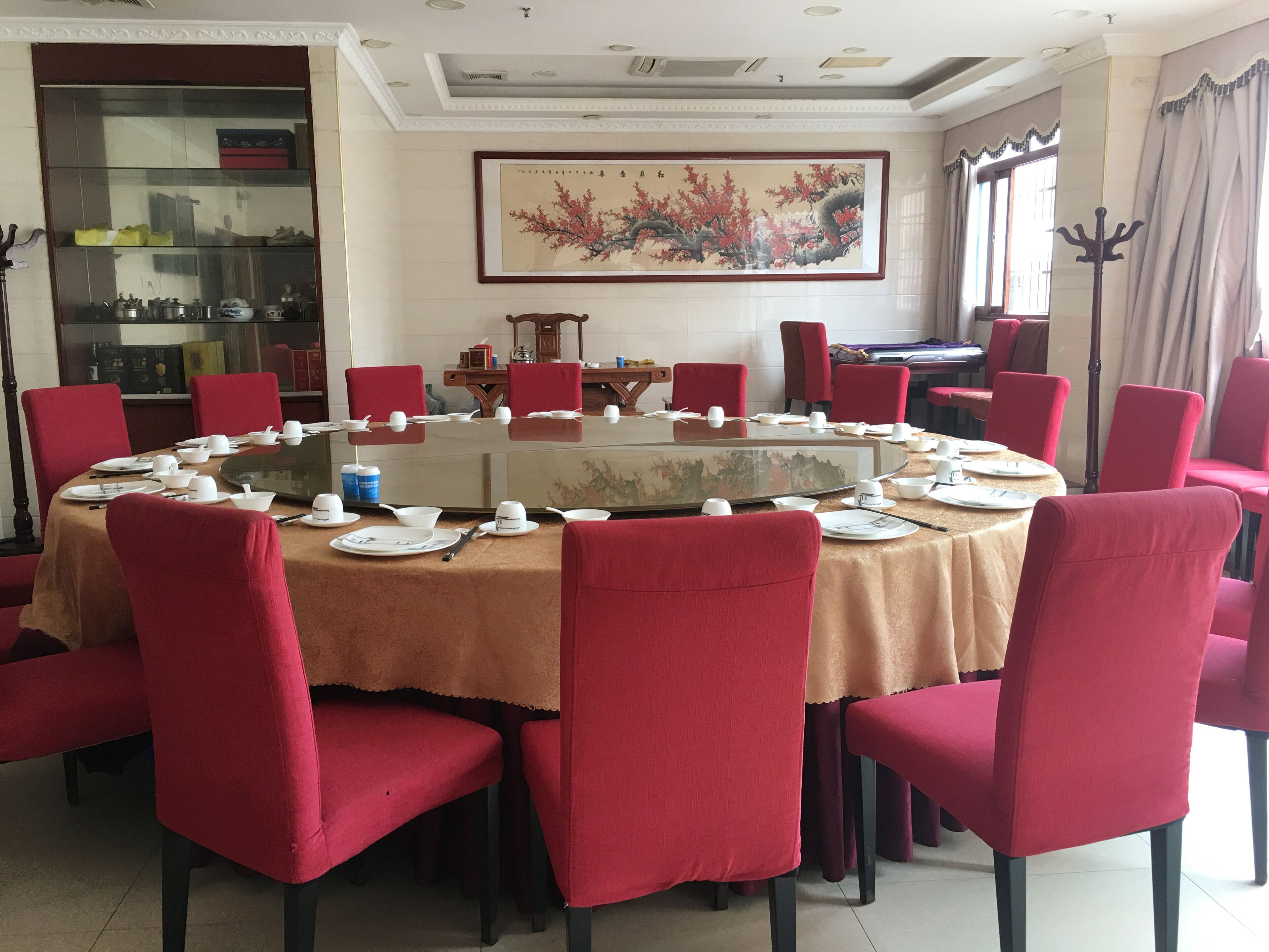 A dining area with a round table, red chairs, and a large painting on the wall.