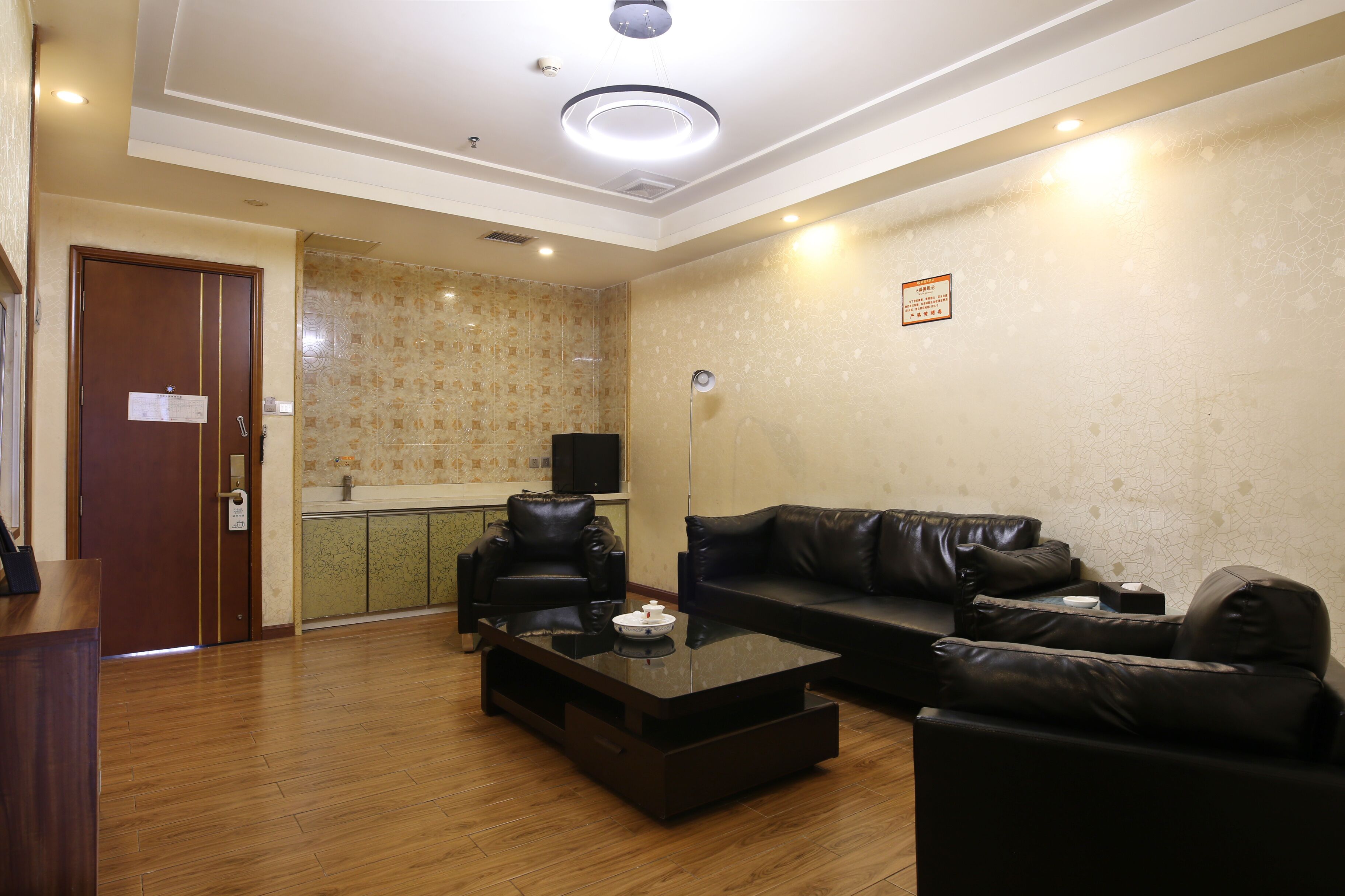 A living room with a wooden floor, a black leather sofa, a coffee table, and a television.