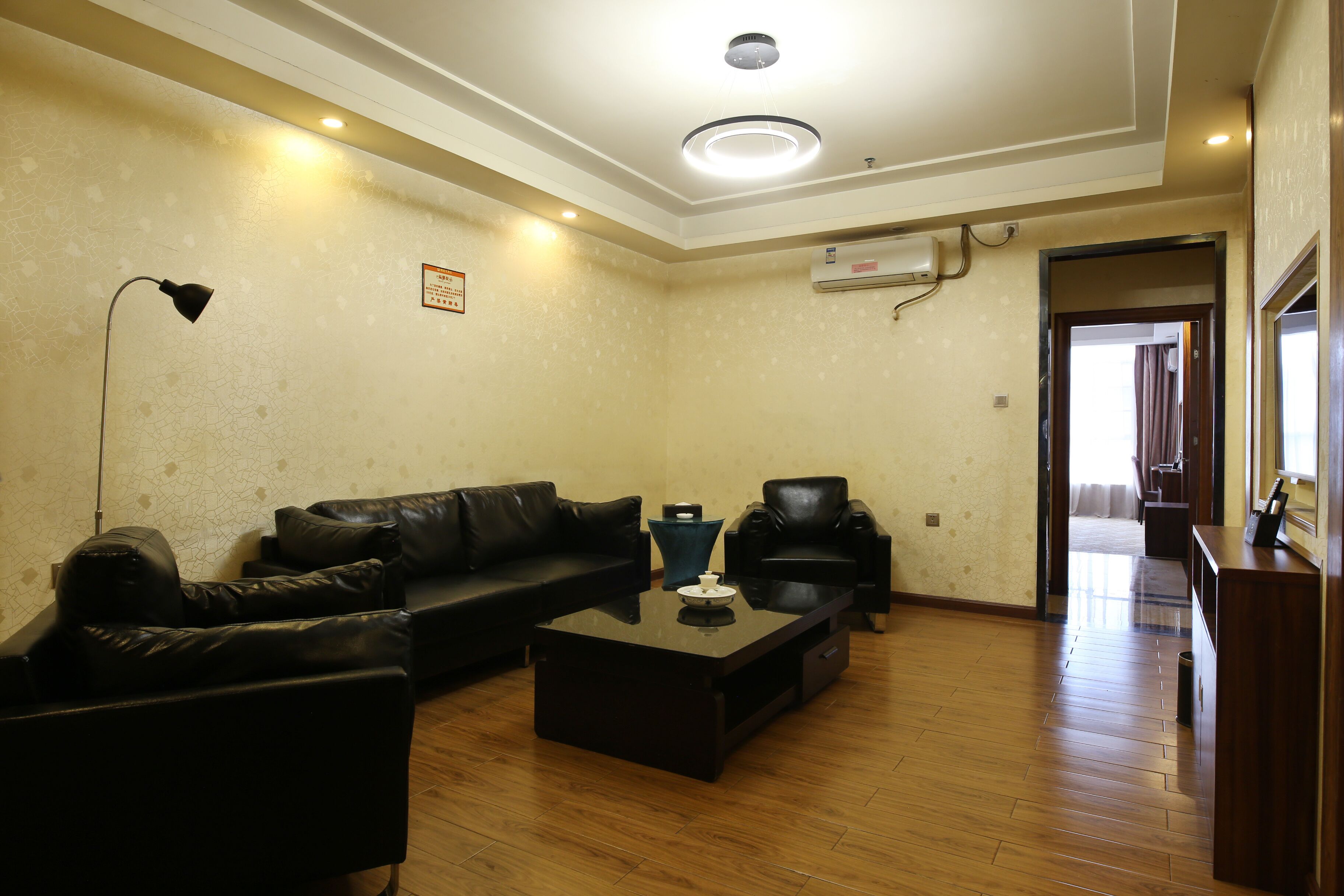 A living room with a black leather sofa, a coffee table, a black armchair, and a wooden floor.