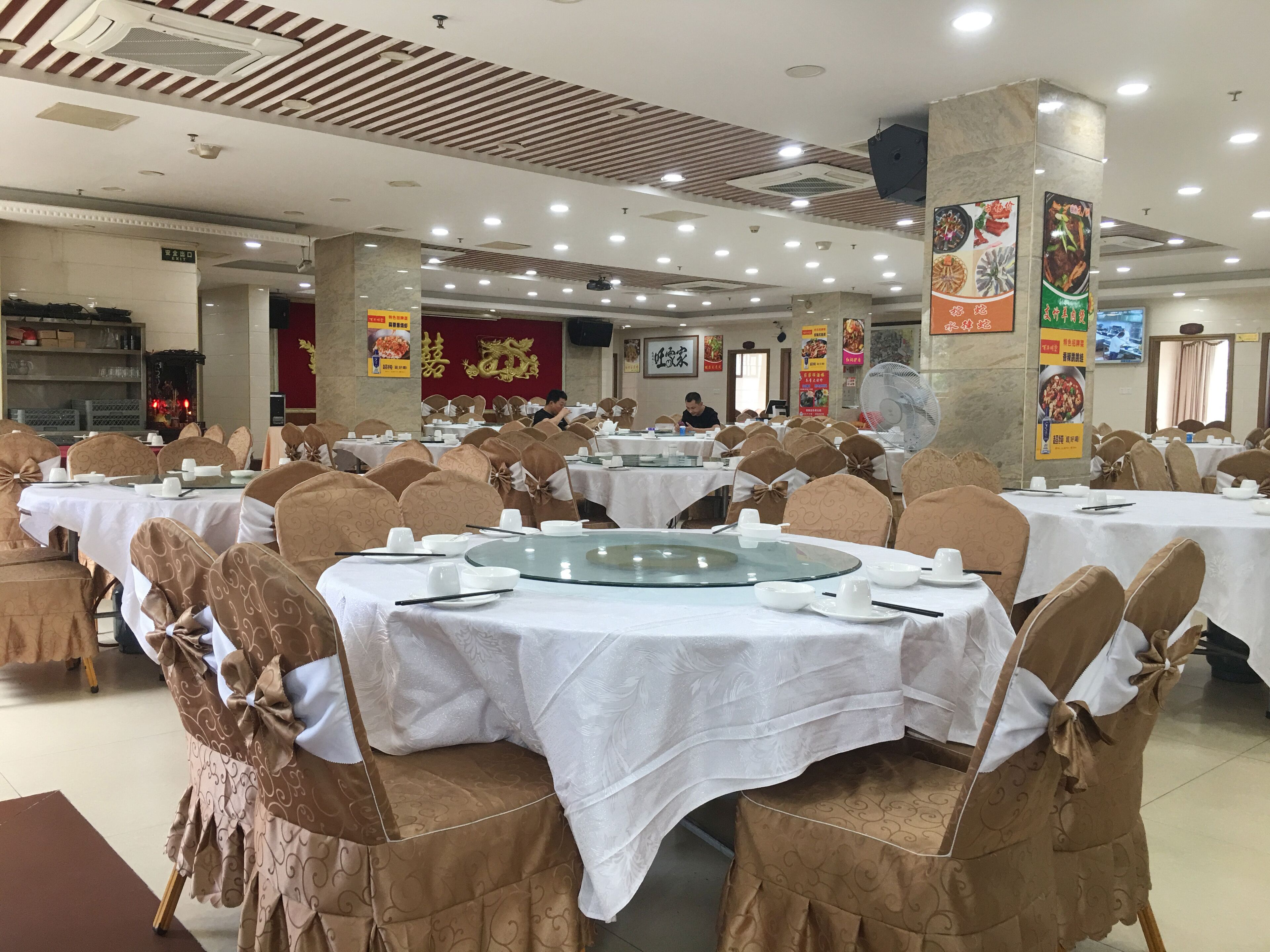 A banquet hall with round tables covered in white tablecloths, arranged in rows.