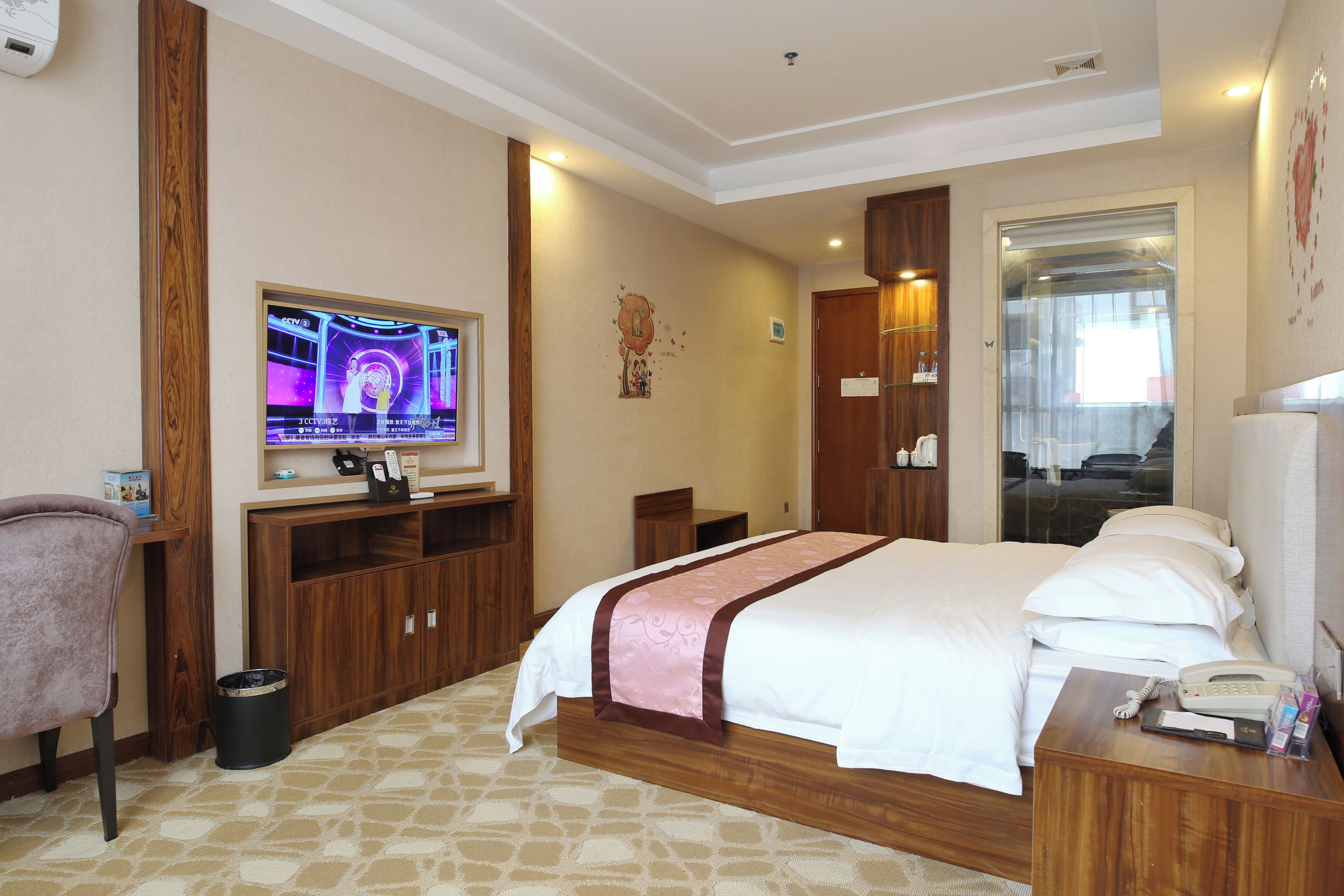 Une chambre d’hôtel avec un grand lit, une télévision, un bureau en bois et une poubelle.
