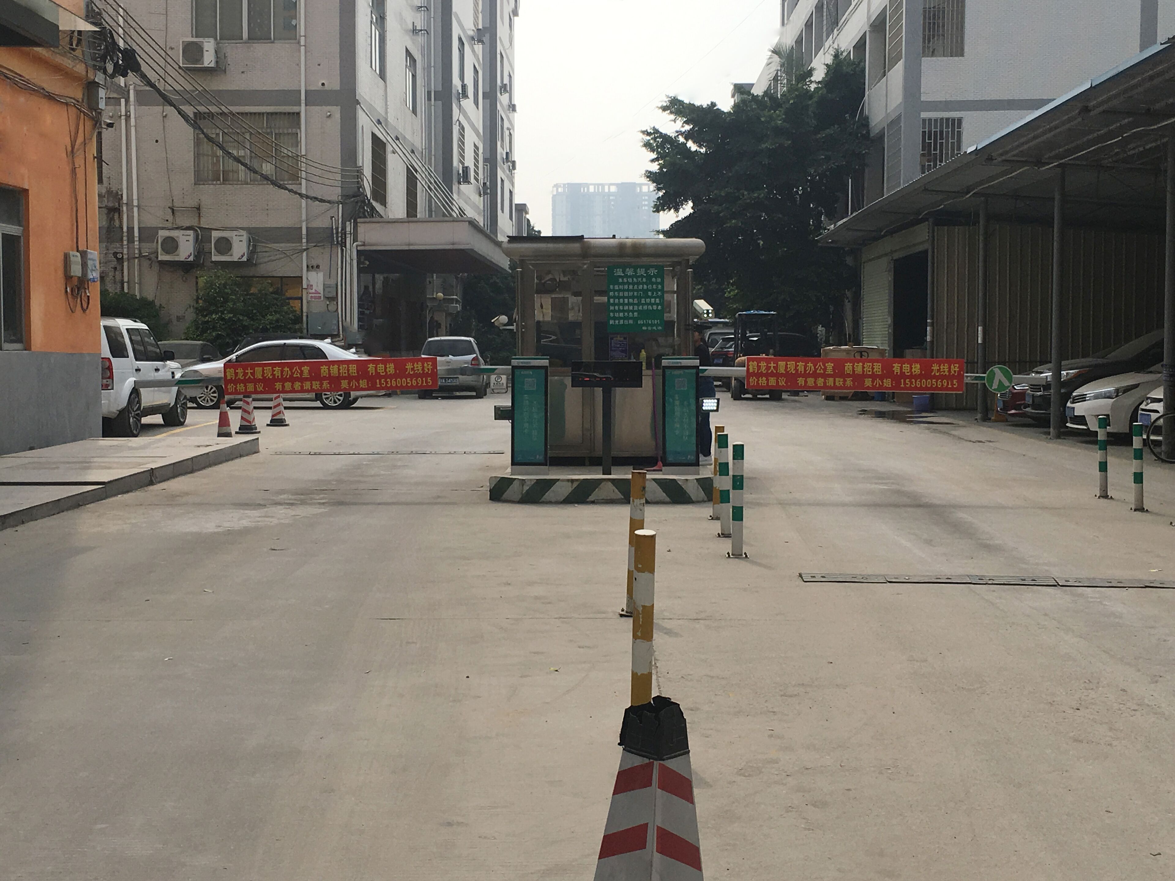Vista da rua com entrada de edifício, uma barreira e vários carros estacionados.