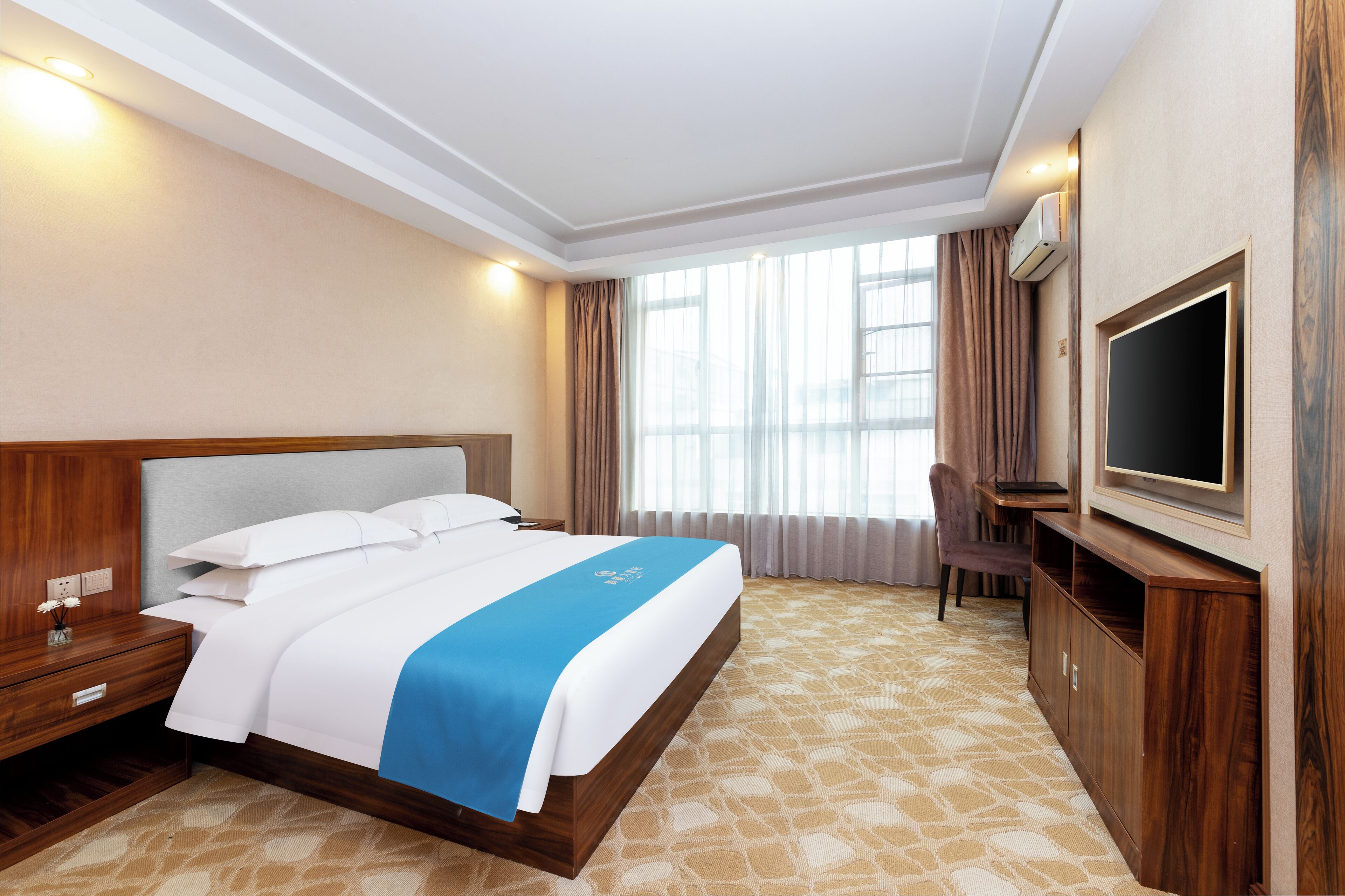 Ein Hotelzimmer mit einem großen Bett, einem an der Wand befestigten Fernseher, einem Schreibtisch und einem Sessel.