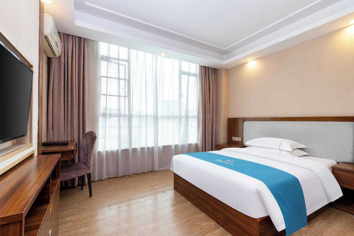 Een hotelkamer met een bed, een bureau, een stoel, een televisie en een raam met gordijnen.
