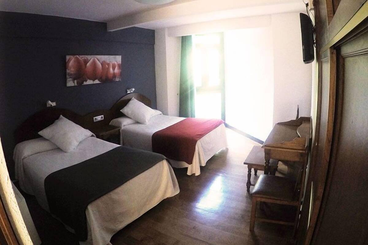 Una habitación de hotel con dos camas, un escritorio y una ventana con cortinas.