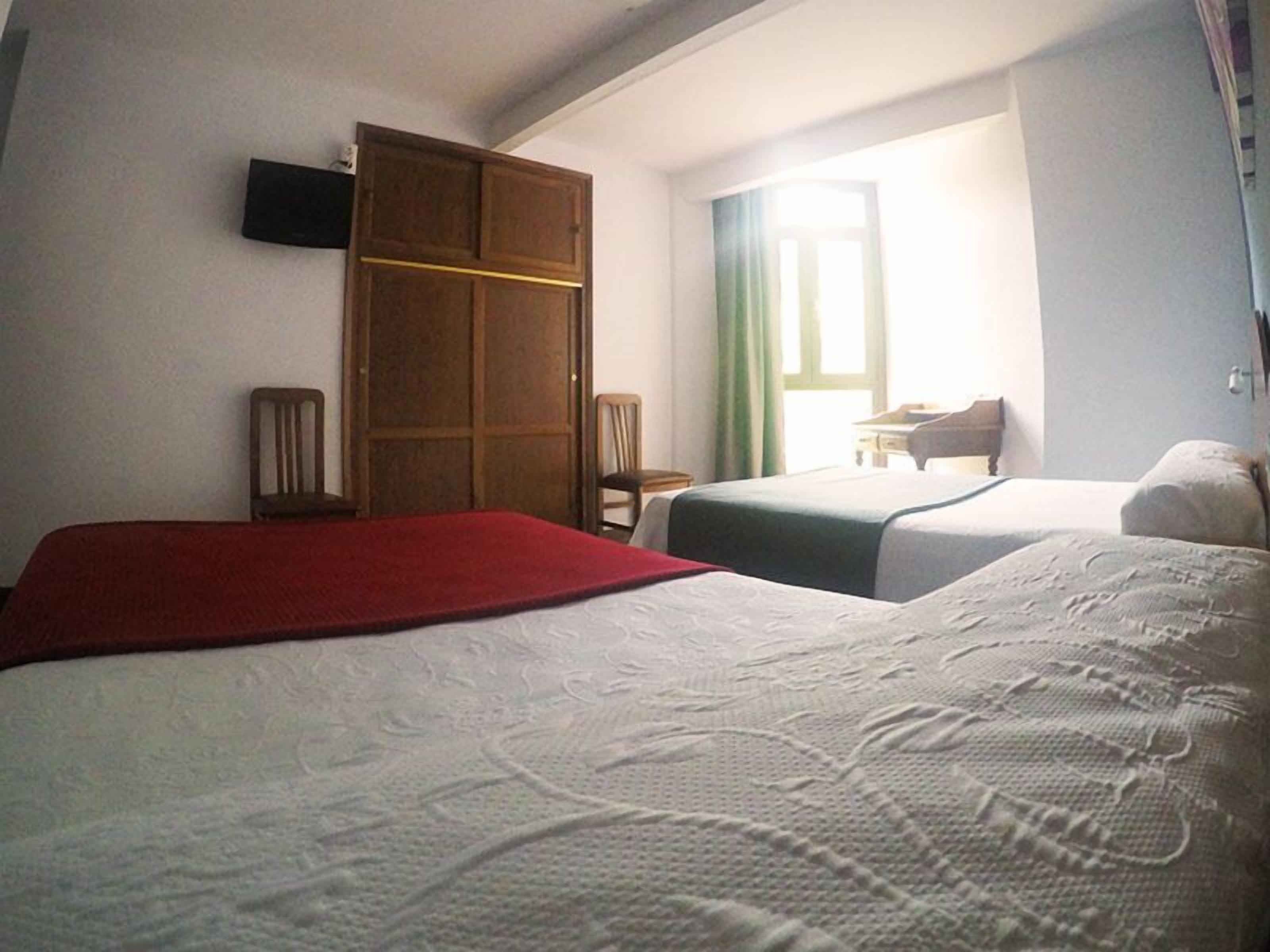 Una camera d'albergo con due letti, un armadio in legno, una scrivania e una sedia.
