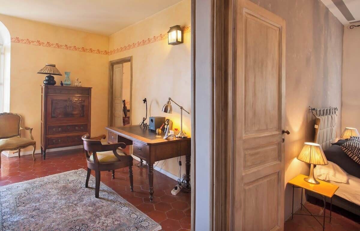 Ein Zimmer mit Holzschreibtisch, zwei Stühlen, einer Lampe, einem Bett mit Nachttisch und einem Kleiderschrank.