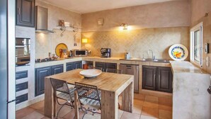 A modern kitchen with dark cabinets, a wooden dining table, and a built-in oven. - Villa A Ventosa (Bastia)