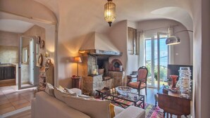 A cozy living room with a fireplace, a sofa, and a dining area with a table and chairs. - Villa A Ventosa (Bastia)