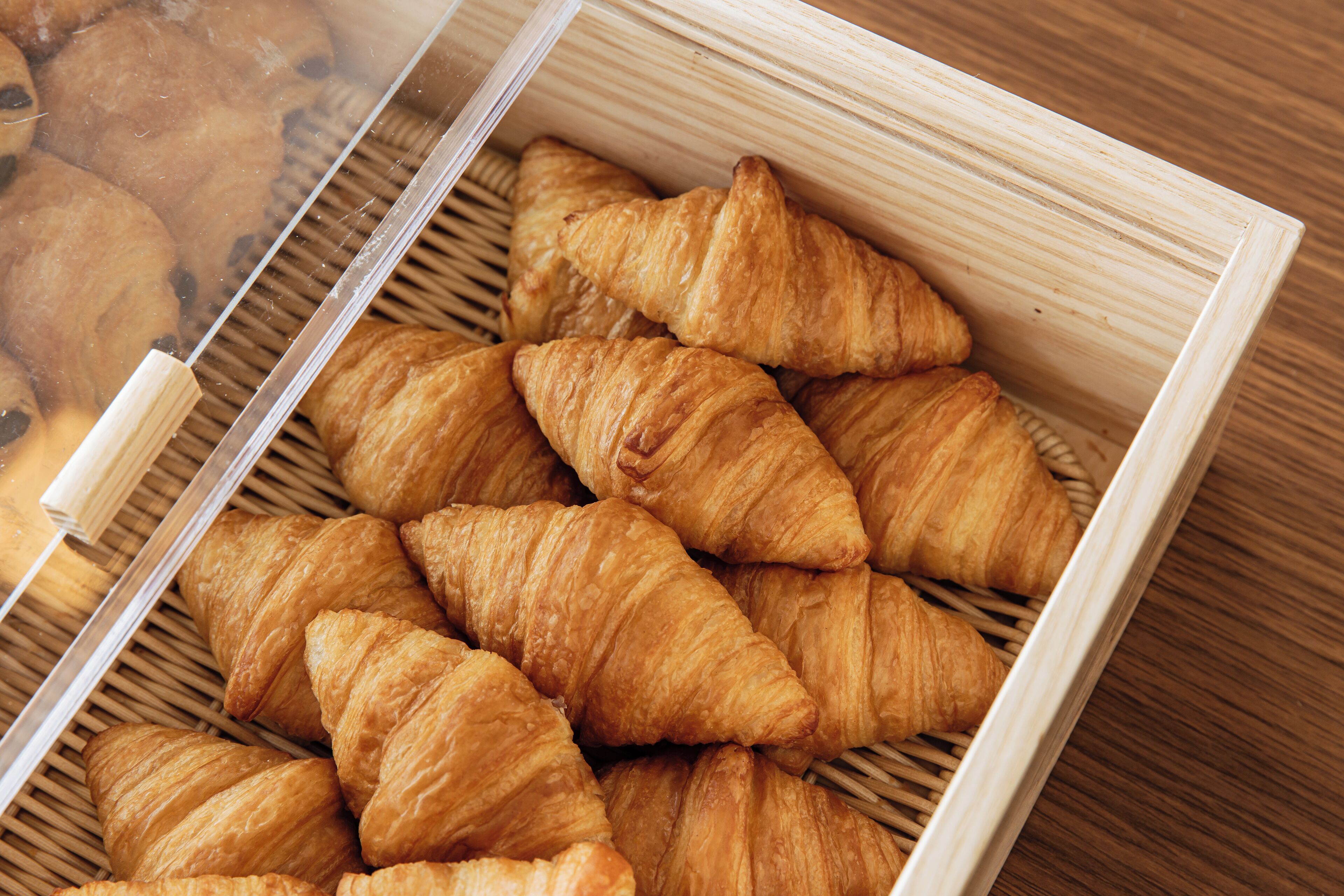 A wooden box containing several golden-brown croissants.