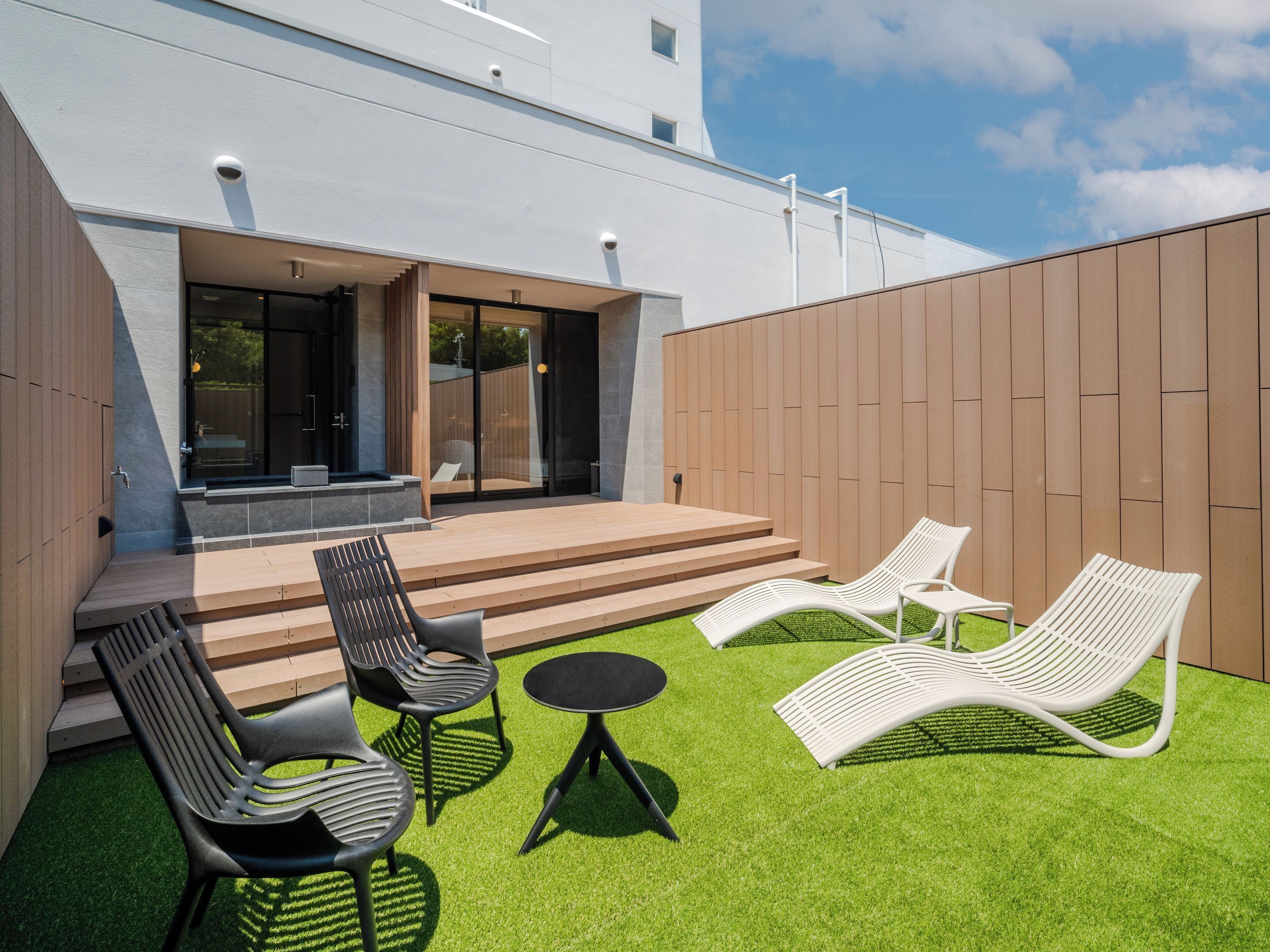 A modern outdoor patio with a wooden deck, a small table, and two lounge chairs.