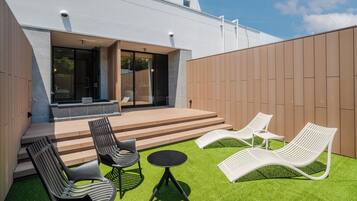 A modern outdoor patio with a wooden deck, a small table, and two lounge chairs.