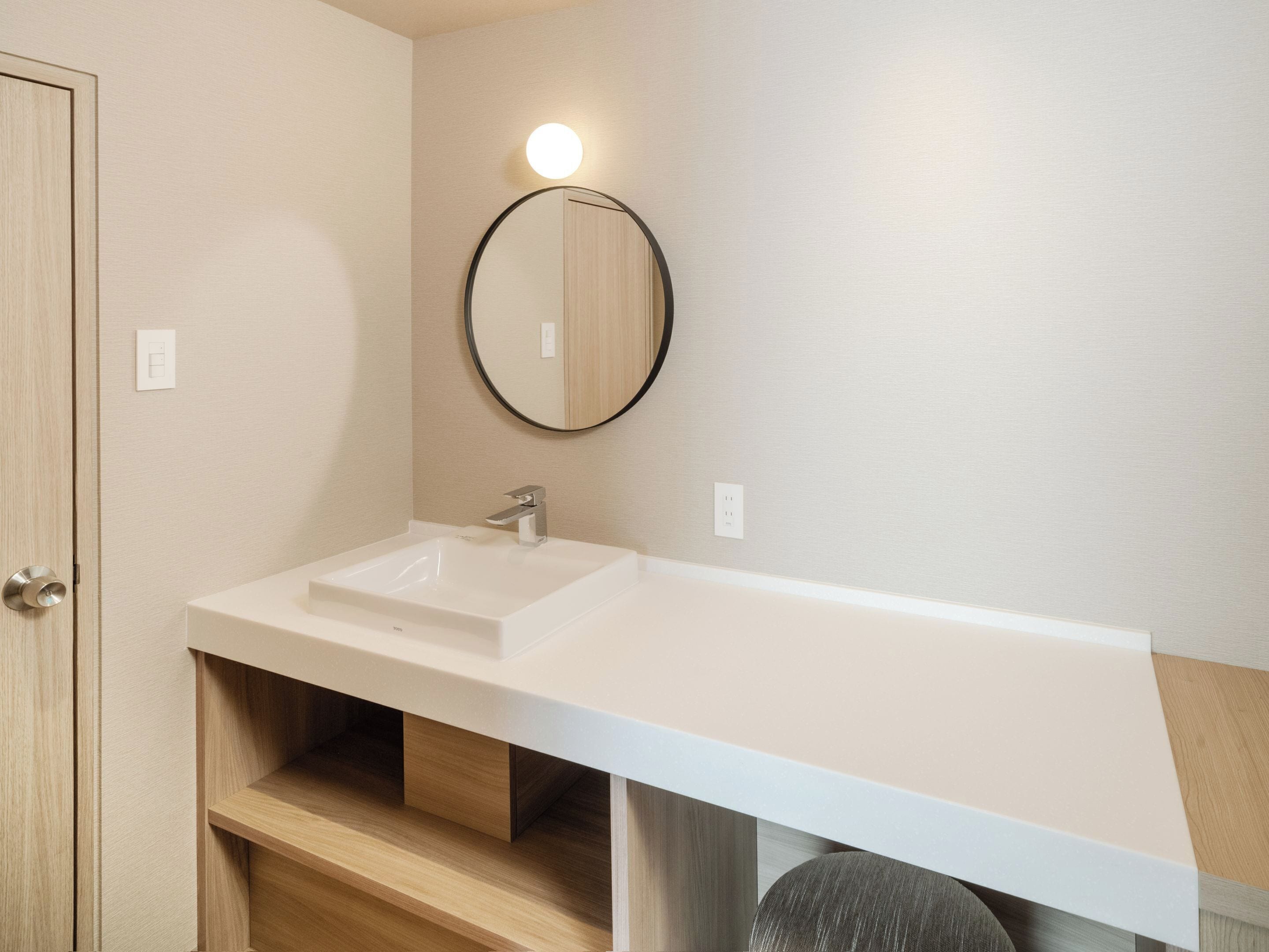 Un bagno con un lavandino bianco, uno specchio rotondo e un armadietto in legno.