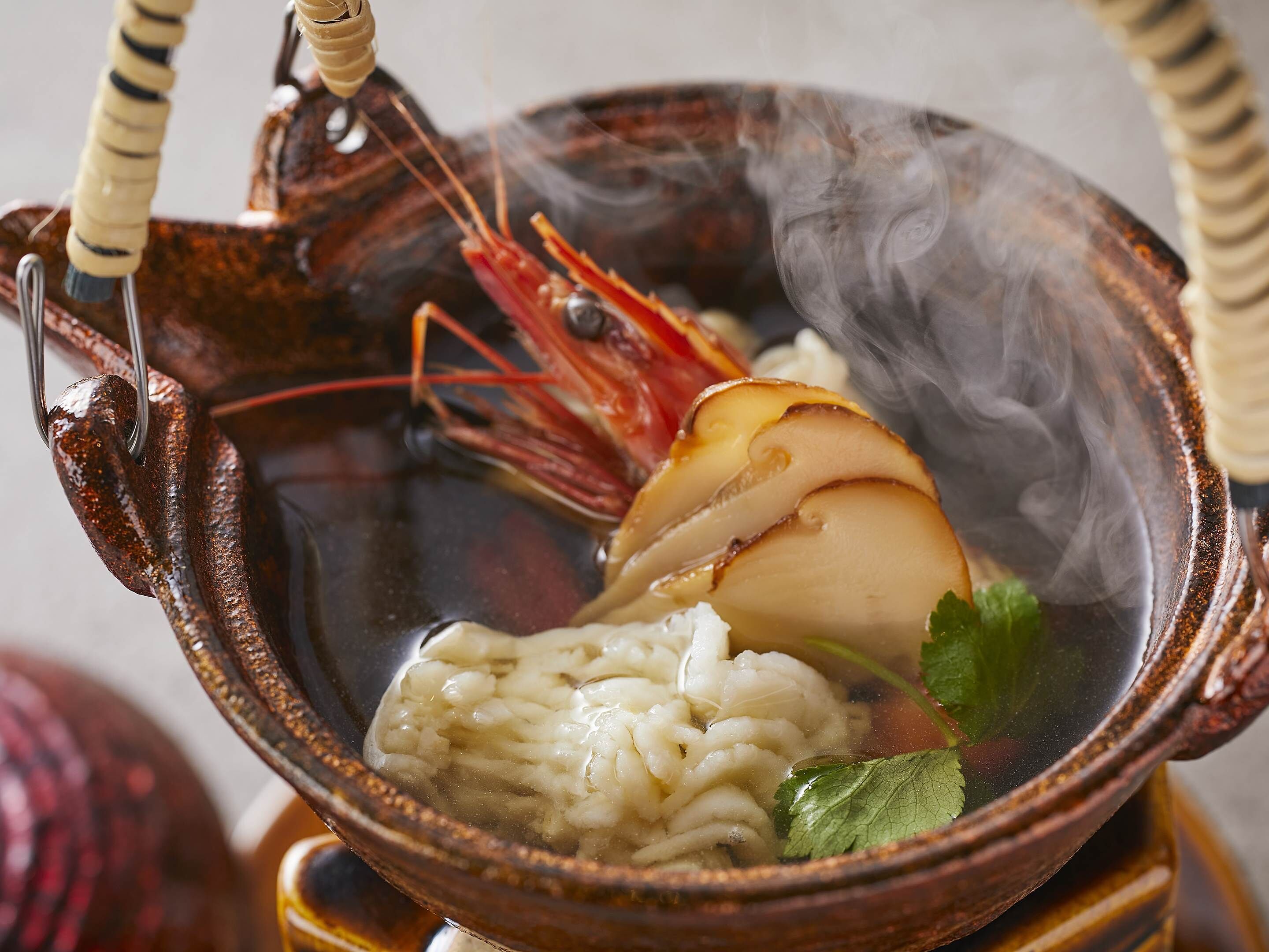 A bowl of soup with noodles, a shrimp, and a slice of meat, served in a ceramic bowl with handles.