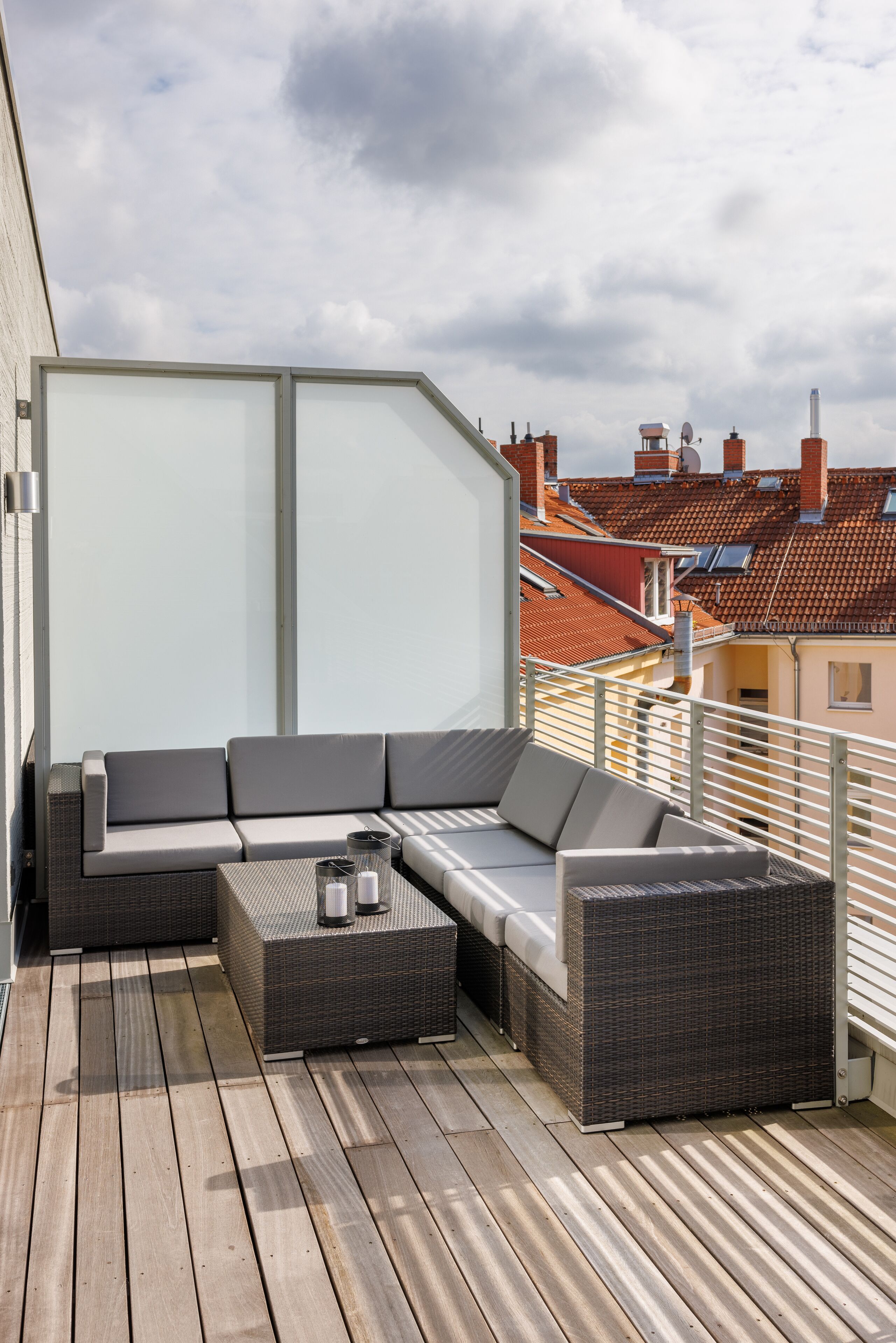 A balcony with a grey sectional sofa, a wicker coffee table, and a glass partition.